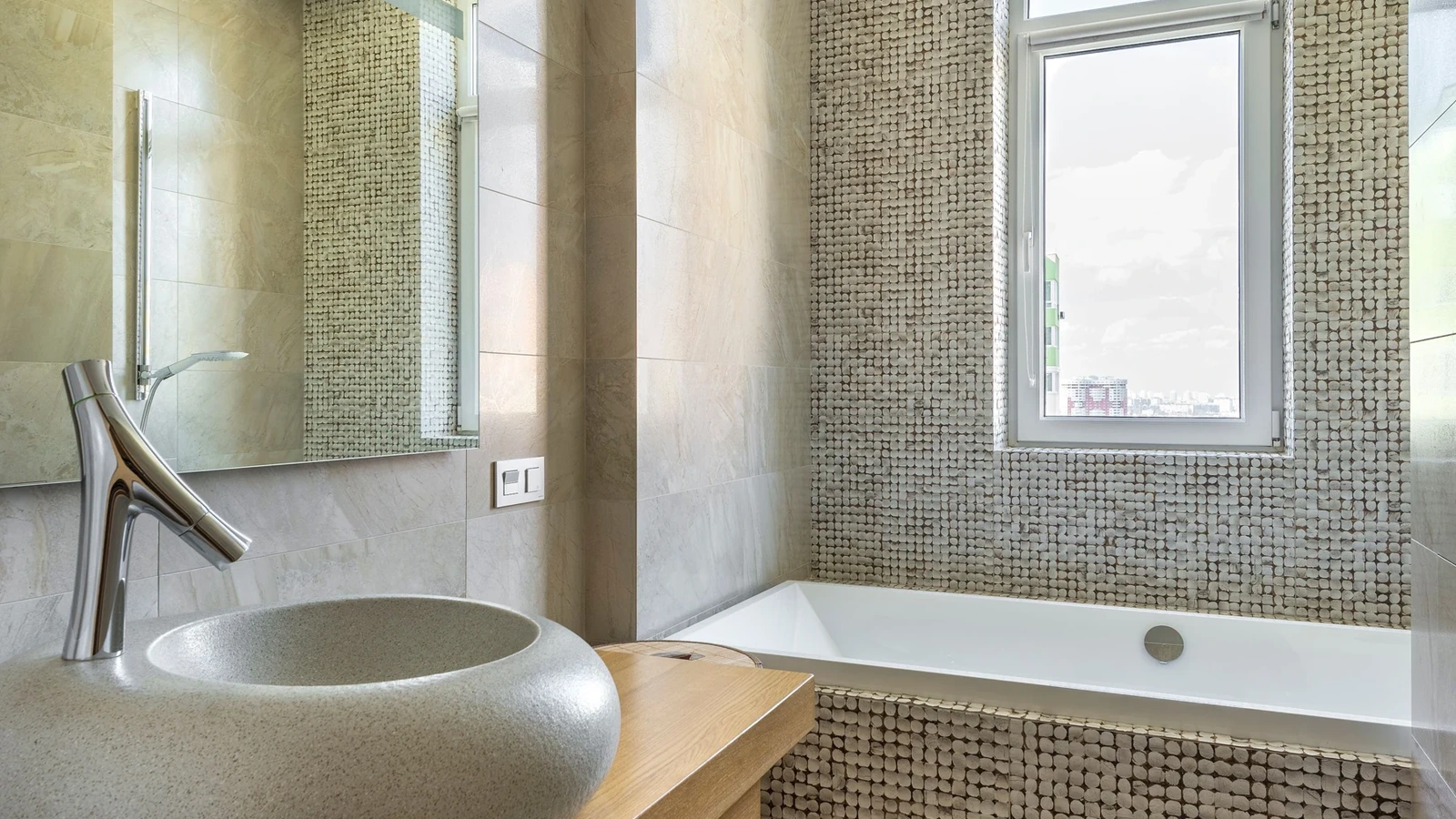Bathroom with small mosaic tiles, an oval vessel basin and an inset bathtub below a window.