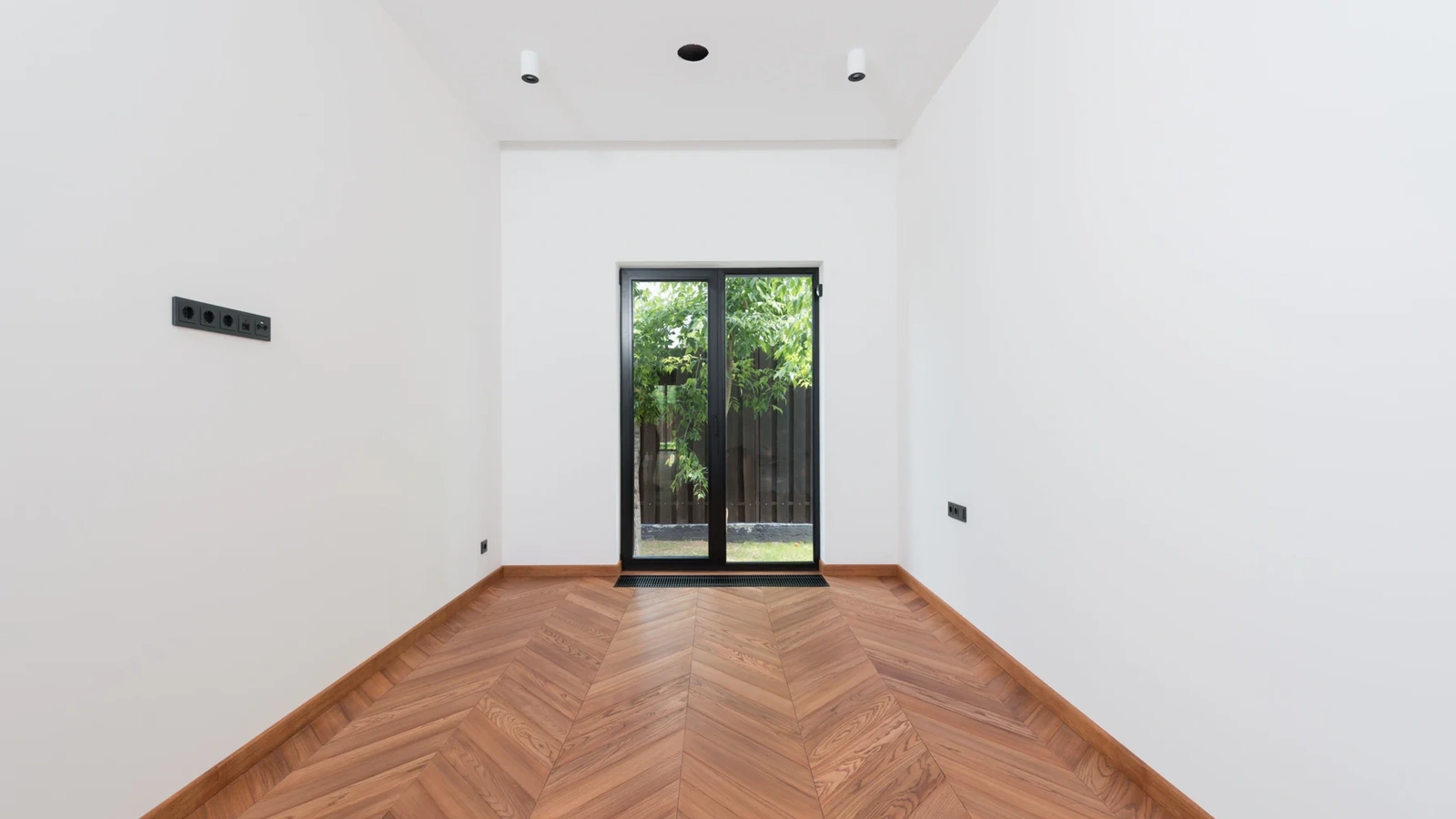 Bright room with white walls, warm herringbone flooring and a glass door.