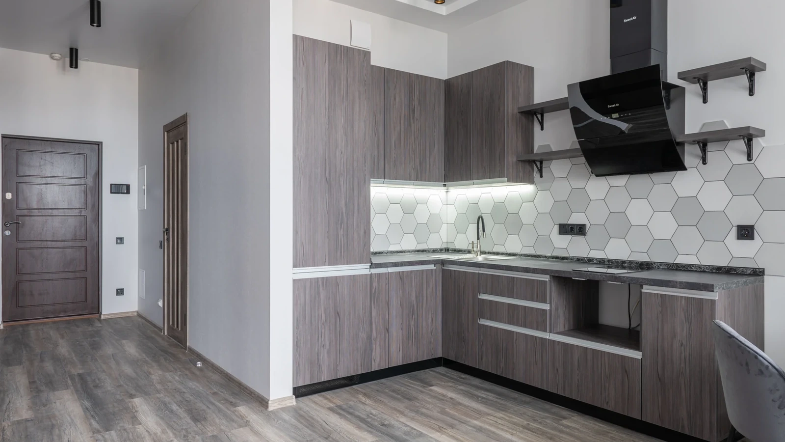Gray wood-look kitchen cabinetry with a white hexagonal backsplash and dark range hood.