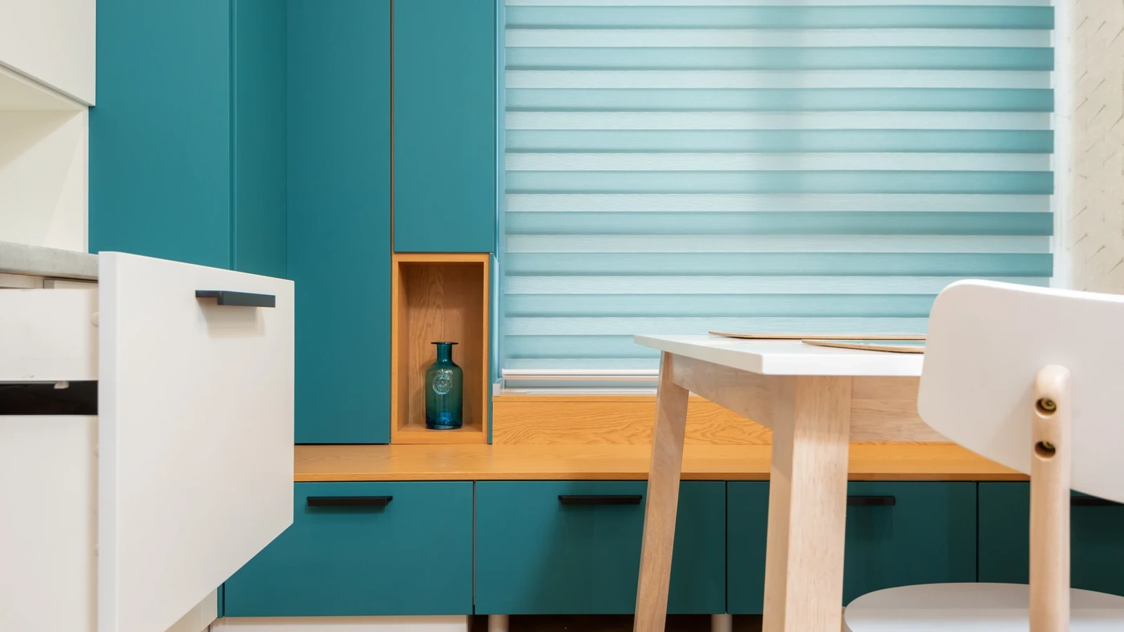 Teal kitchen cabinets and an open white drawer beside a warm wood work surface.