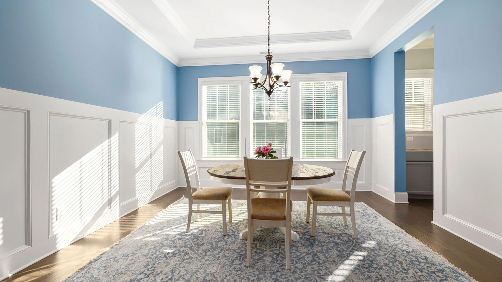 Light blue dining room with white trim, large windows and a wooden dining table.