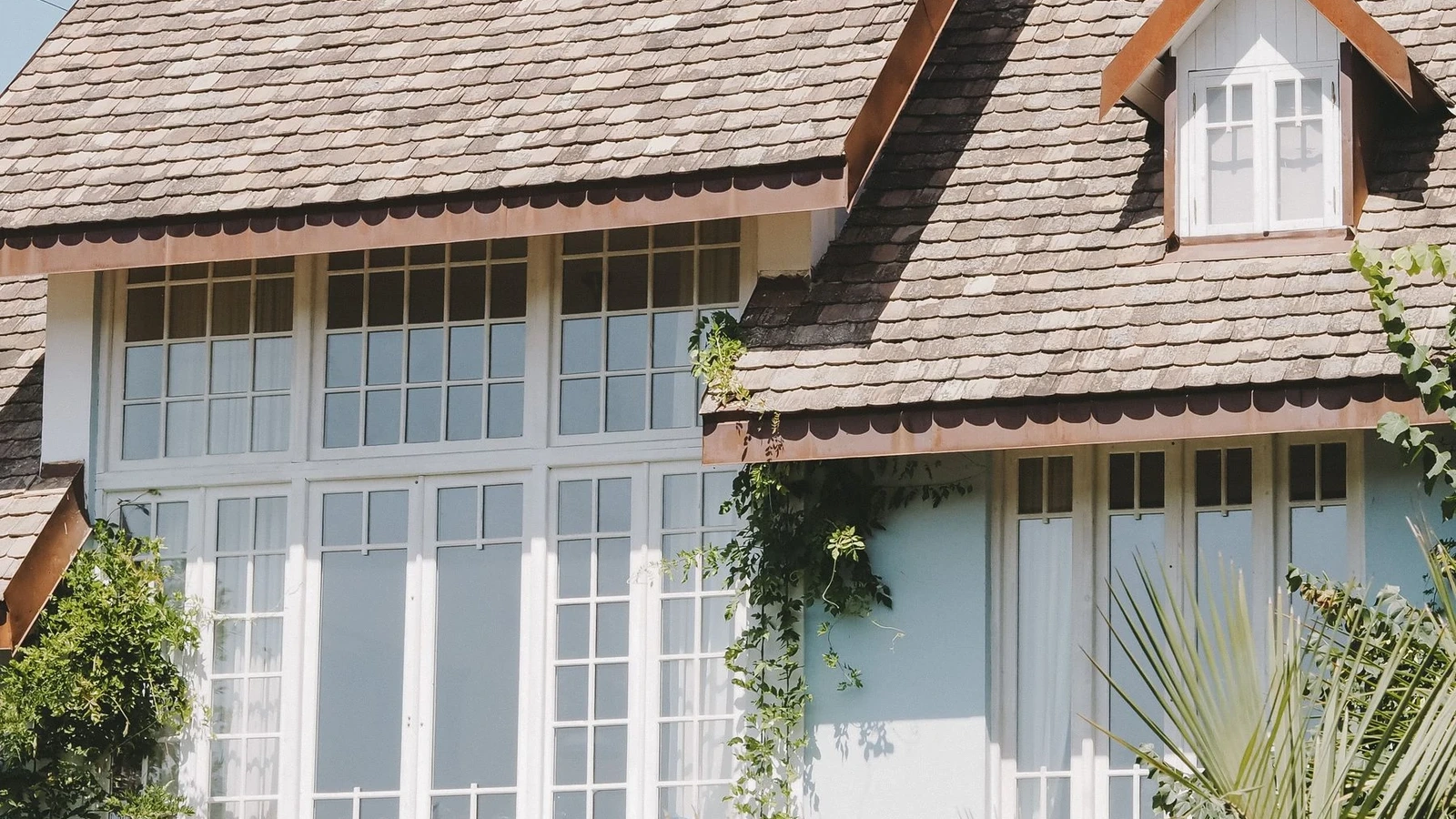 Large white divided-light windows beneath a steep shingled roof in sunlight.